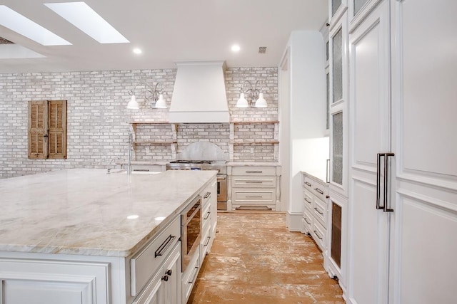 kitchen with sink, premium range hood, white cabinetry, stainless steel appliances, and light stone counters