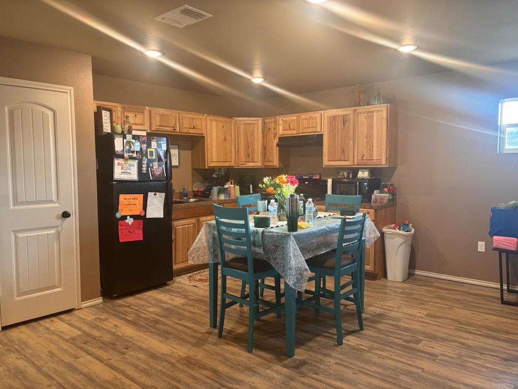 kitchen with wood-type flooring, black fridge, and light brown cabinets