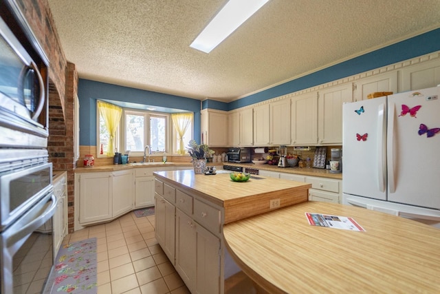 kitchen with sink, a center island, a textured ceiling, light tile patterned floors, and stainless steel appliances