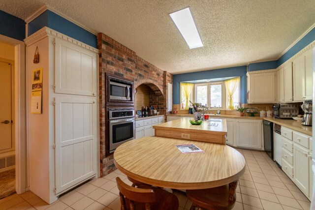 kitchen with appliances with stainless steel finishes, white cabinetry, a skylight, a textured ceiling, and light tile patterned flooring