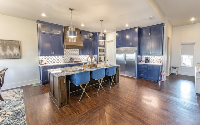 kitchen with built in appliances, a kitchen bar, light stone counters, blue cabinets, and a kitchen island with sink