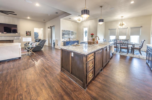 kitchen featuring an island with sink, a barn door, light stone countertops, sink, and pendant lighting