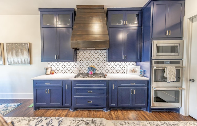 kitchen with stainless steel appliances, blue cabinets, premium range hood, backsplash, and dark hardwood / wood-style floors