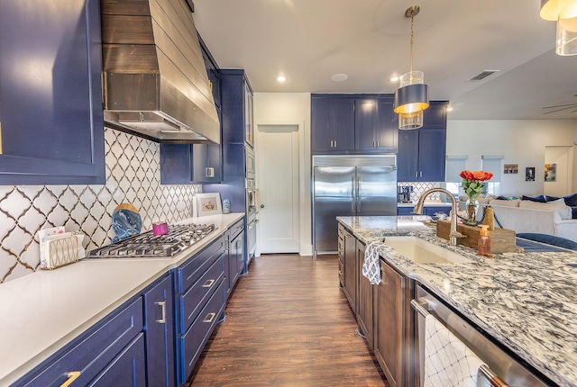 kitchen featuring hanging light fixtures, blue cabinetry, stainless steel appliances, custom range hood, and sink