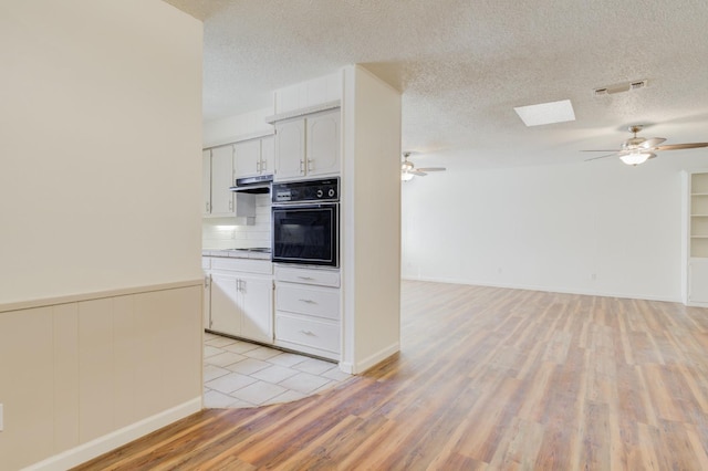 kitchen with white cabinetry, tasteful backsplash, light wood-type flooring, ceiling fan, and oven