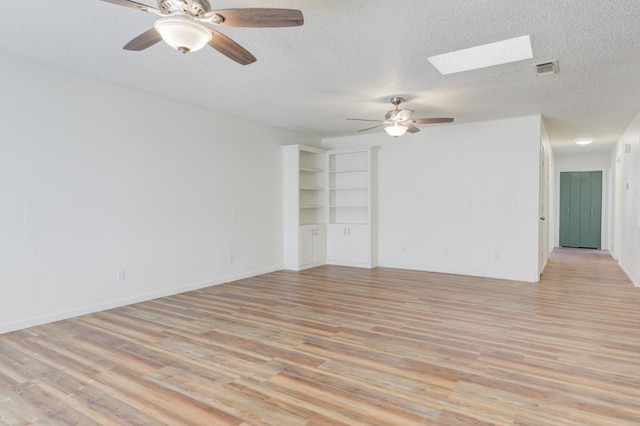 spare room featuring ceiling fan, light hardwood / wood-style flooring, a textured ceiling, and a skylight