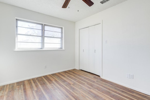 unfurnished bedroom with wood-type flooring, ceiling fan, a textured ceiling, and a closet