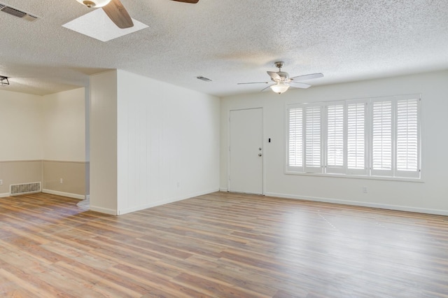 empty room featuring a textured ceiling, a skylight, light hardwood / wood-style floors, and ceiling fan