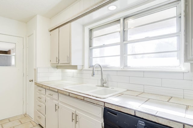 kitchen featuring tile countertops, tasteful backsplash, white cabinetry, black dishwasher, and sink