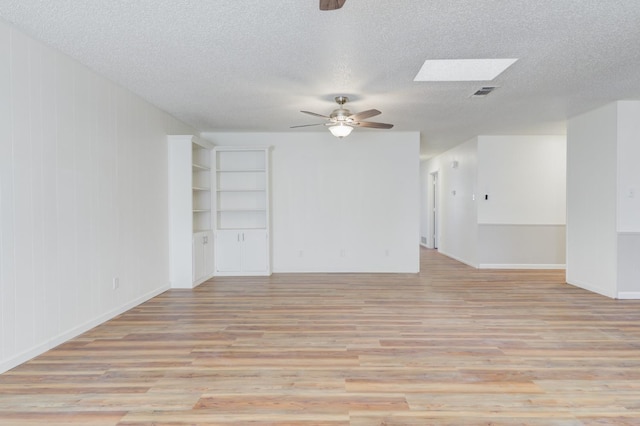 unfurnished room featuring a textured ceiling, a skylight, light hardwood / wood-style floors, and ceiling fan