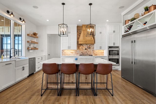 kitchen featuring premium range hood, white cabinetry, a center island, appliances with stainless steel finishes, and hardwood / wood-style flooring