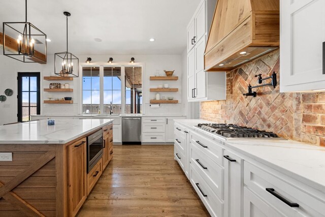 kitchen with a kitchen island, appliances with stainless steel finishes, white cabinetry, light stone counters, and custom range hood