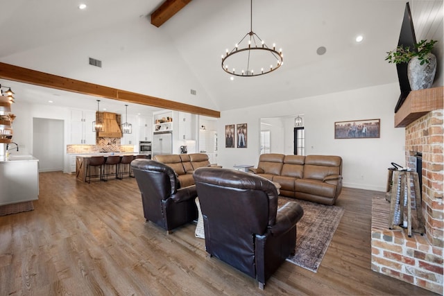 living room with an inviting chandelier, wood-type flooring, sink, a brick fireplace, and beam ceiling