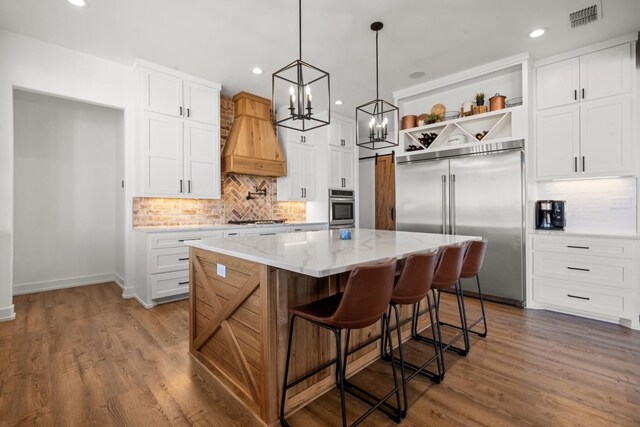 kitchen with white cabinetry, custom exhaust hood, stainless steel appliances, and a kitchen island