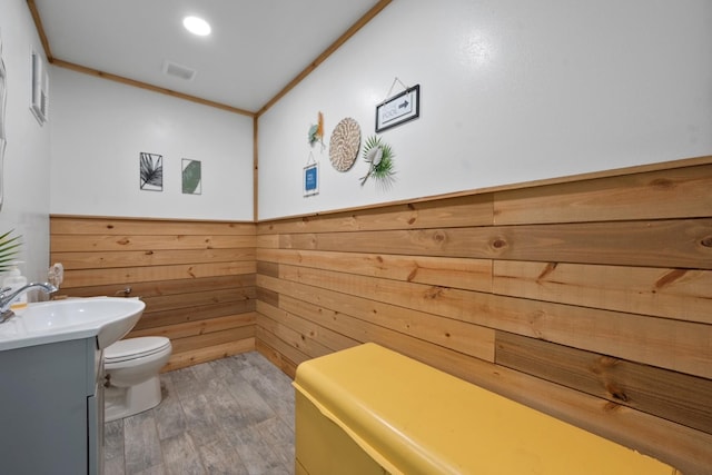 bathroom with hardwood / wood-style flooring, crown molding, vanity, toilet, and wood walls