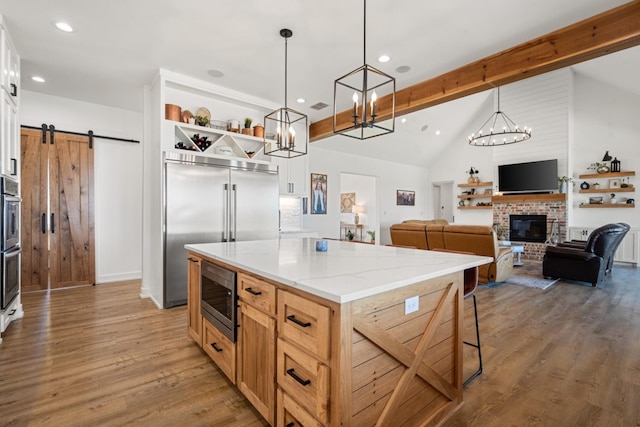 kitchen featuring hanging light fixtures, built in appliances, light stone countertops, a kitchen island, and a barn door