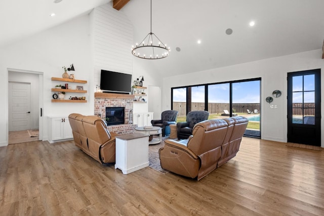 living room featuring high vaulted ceiling, a notable chandelier, a fireplace, and light hardwood / wood-style flooring