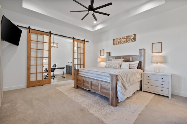 carpeted bedroom with a tray ceiling and a barn door