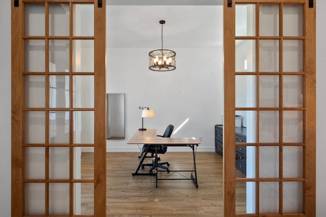 unfurnished office featuring hardwood / wood-style flooring, a barn door, and an inviting chandelier