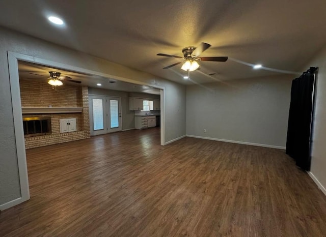 unfurnished living room with a brick fireplace, dark wood-type flooring, ceiling fan, and brick wall