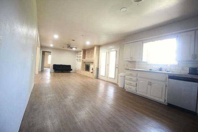 kitchen featuring stainless steel dishwasher, hardwood / wood-style floors, a brick fireplace, and white cabinets