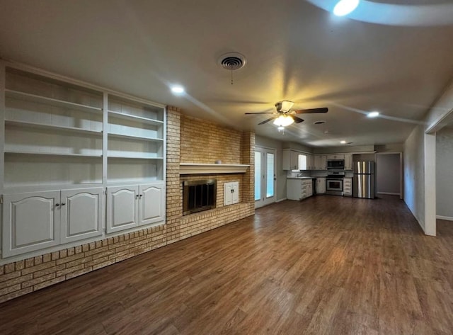 unfurnished living room with brick wall, dark hardwood / wood-style floors, ceiling fan, a brick fireplace, and built in shelves