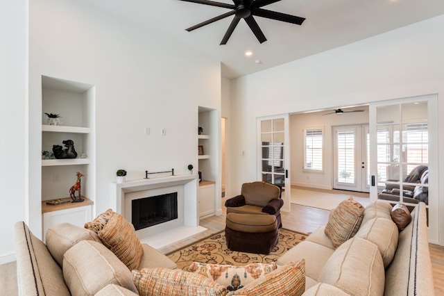 living room with built in shelves, light hardwood / wood-style floors, and ceiling fan