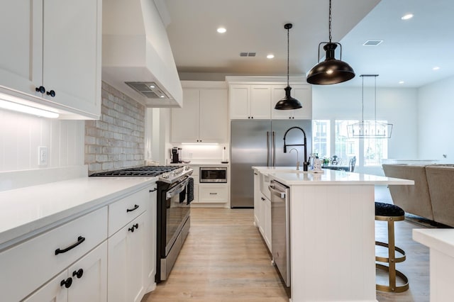 kitchen with premium range hood, white cabinets, a kitchen bar, hanging light fixtures, and built in appliances