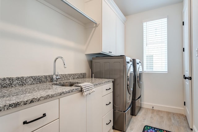 clothes washing area featuring cabinets, washing machine and dryer, sink, and light hardwood / wood-style flooring