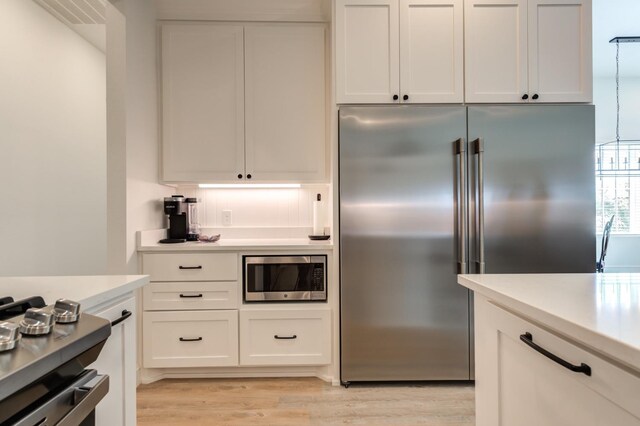 kitchen with built in appliances, white cabinetry, and light hardwood / wood-style floors