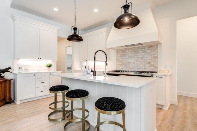 kitchen featuring white cabinetry, an island with sink, hanging light fixtures, and custom range hood