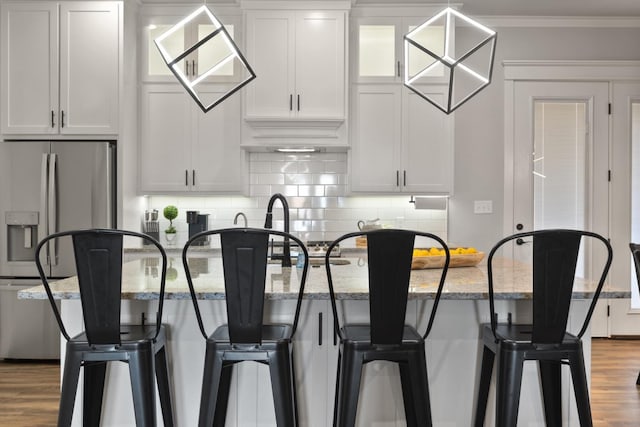 kitchen with tasteful backsplash, white cabinets, a kitchen breakfast bar, stainless steel fridge, and light stone counters