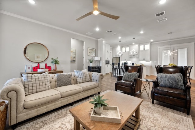 living room featuring ceiling fan with notable chandelier, ornamental molding, and light hardwood / wood-style floors