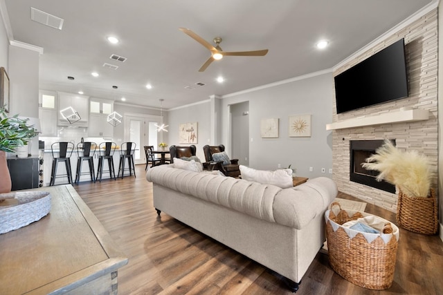 living room featuring ceiling fan, dark wood-type flooring, crown molding, and a fireplace