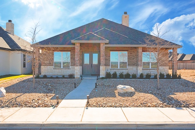 view of front of property featuring stone siding, a chimney, and a shingled roof