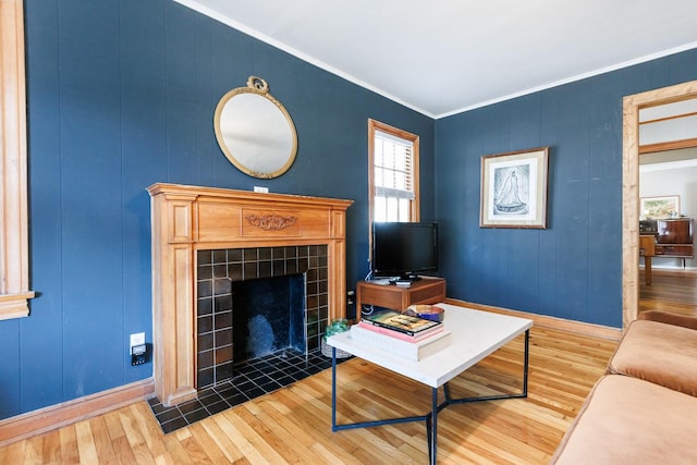 living room with a tiled fireplace, wood-type flooring, and crown molding