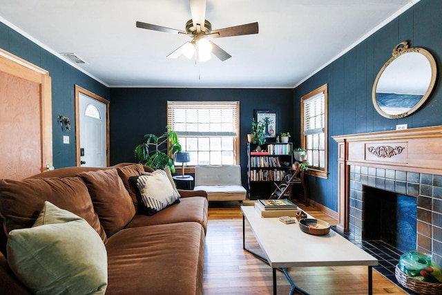 living room featuring a tile fireplace, wood-type flooring, ceiling fan, and crown molding