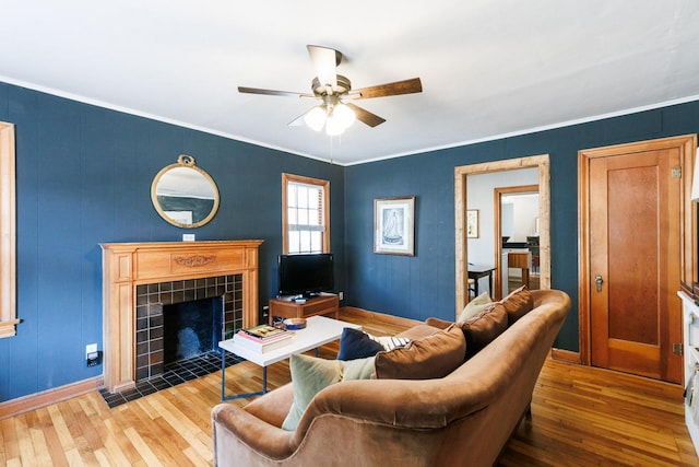 living room featuring a tile fireplace, ornamental molding, hardwood / wood-style floors, and ceiling fan