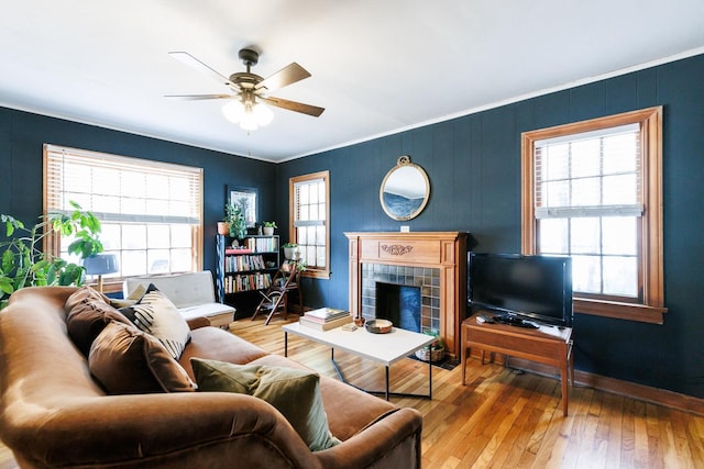 living room with crown molding, a tile fireplace, light hardwood / wood-style floors, and ceiling fan