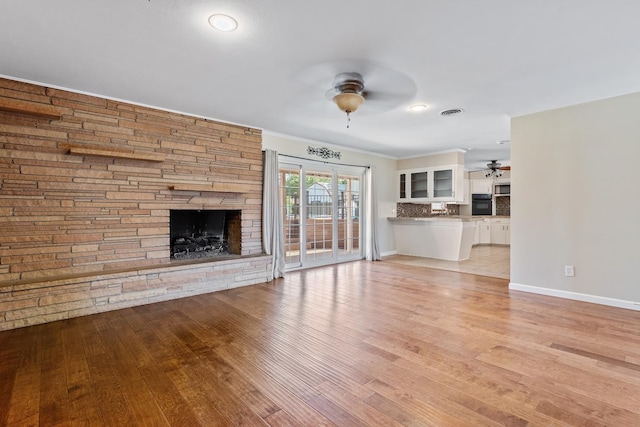 unfurnished living room with crown molding, a stone fireplace, ceiling fan, and light wood-type flooring