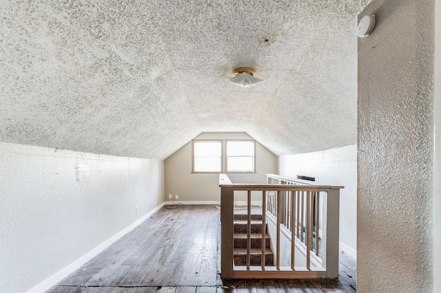 additional living space featuring hardwood / wood-style flooring, vaulted ceiling, and a textured ceiling