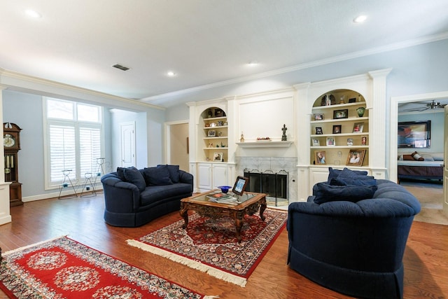 living room with a tiled fireplace, crown molding, dark hardwood / wood-style floors, and built in shelves