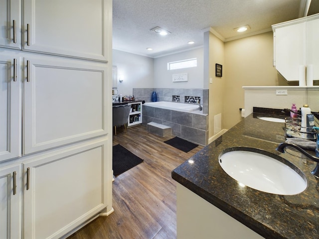 bathroom with a textured ceiling, hardwood / wood-style flooring, ornamental molding, vanity, and a relaxing tiled tub