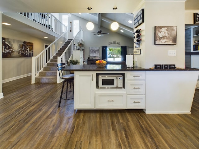 kitchen with high vaulted ceiling, white cabinetry, a breakfast bar area, hanging light fixtures, and dark wood-type flooring