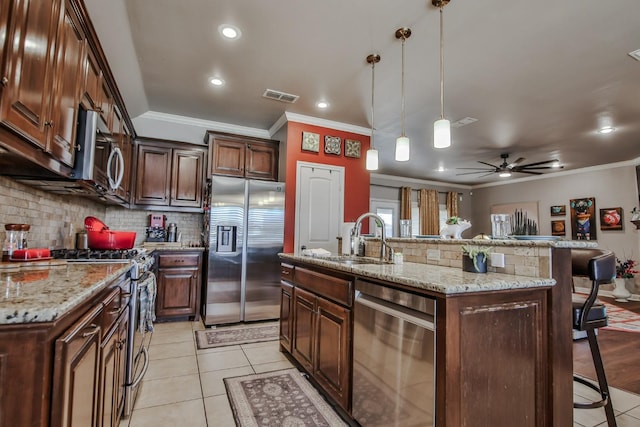 kitchen featuring decorative light fixtures, sink, a breakfast bar area, stainless steel appliances, and a center island with sink