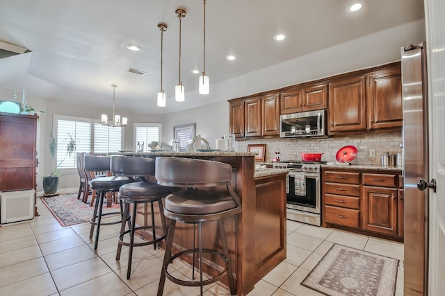 kitchen with a breakfast bar area, an island with sink, pendant lighting, stainless steel appliances, and light stone countertops