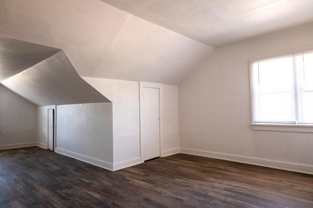 additional living space with dark hardwood / wood-style floors, vaulted ceiling, and a textured ceiling