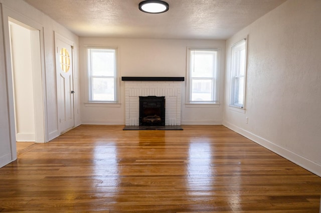 unfurnished living room with a brick fireplace, a textured ceiling, and dark hardwood / wood-style flooring