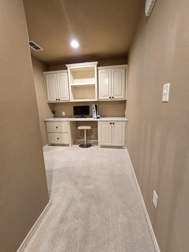 unfurnished office featuring built in desk and light colored carpet