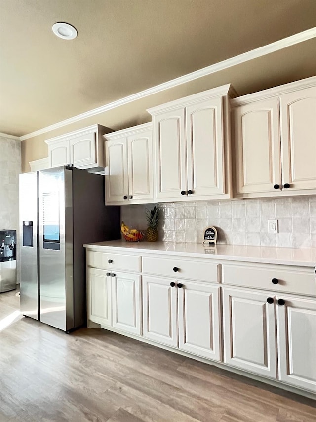 kitchen with stainless steel refrigerator with ice dispenser, crown molding, light wood-type flooring, white cabinets, and backsplash